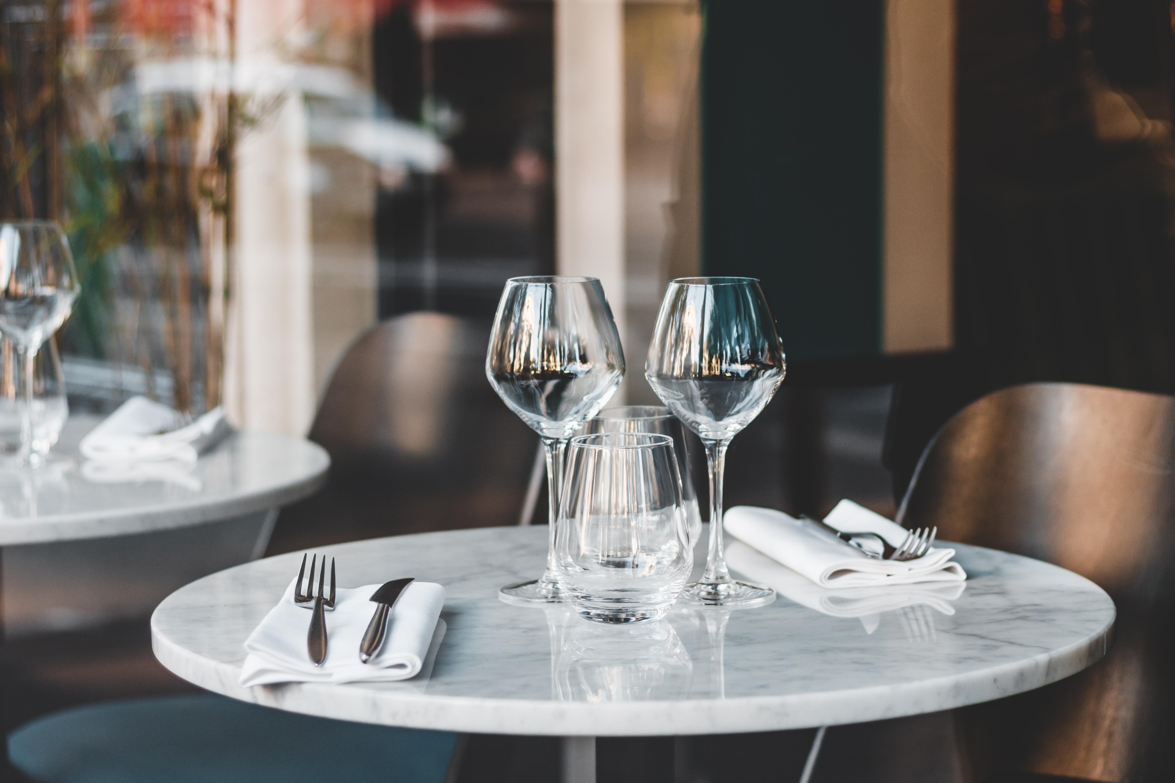 Ein elegant gedeckter runder Marmortisch in einem Restaurant mit Weingläsern, Besteck auf weißen Servietten und dunklen Holzstühlen.