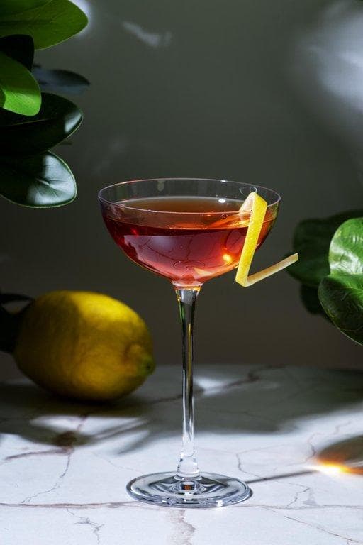 Weinbar Bregenz: bernsteinfarbener Cocktail in flacher Sektschale mit Zitronenzeste auf Marmoruntergrund.