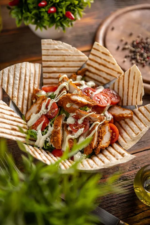 Knusprige Hähnchenstreifen mit Kirschtomaten und Sauce, serviert in einer Schale aus gegrillten Tortilla-Stücken.