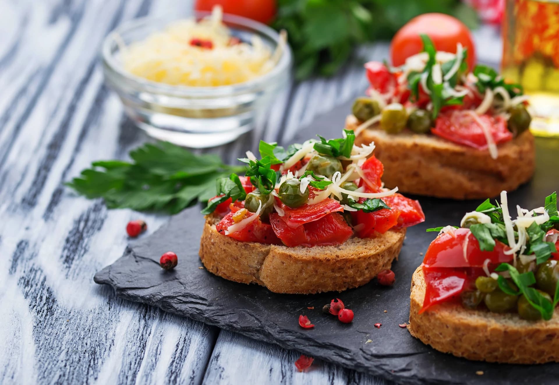 Knusprige Bruschetta-Scheiben belegt mit gewürfelten Tomaten, frischen Kräutern, Kapern und geriebenem Käse.