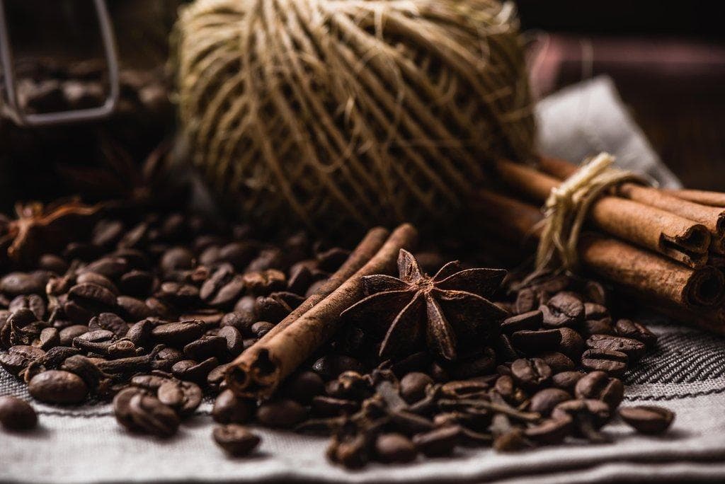 Geröstete Kaffeebohnen mit Zimtstangen und Sternanis auf einem Leinentuch neben einem Knäuel Küchengarn.