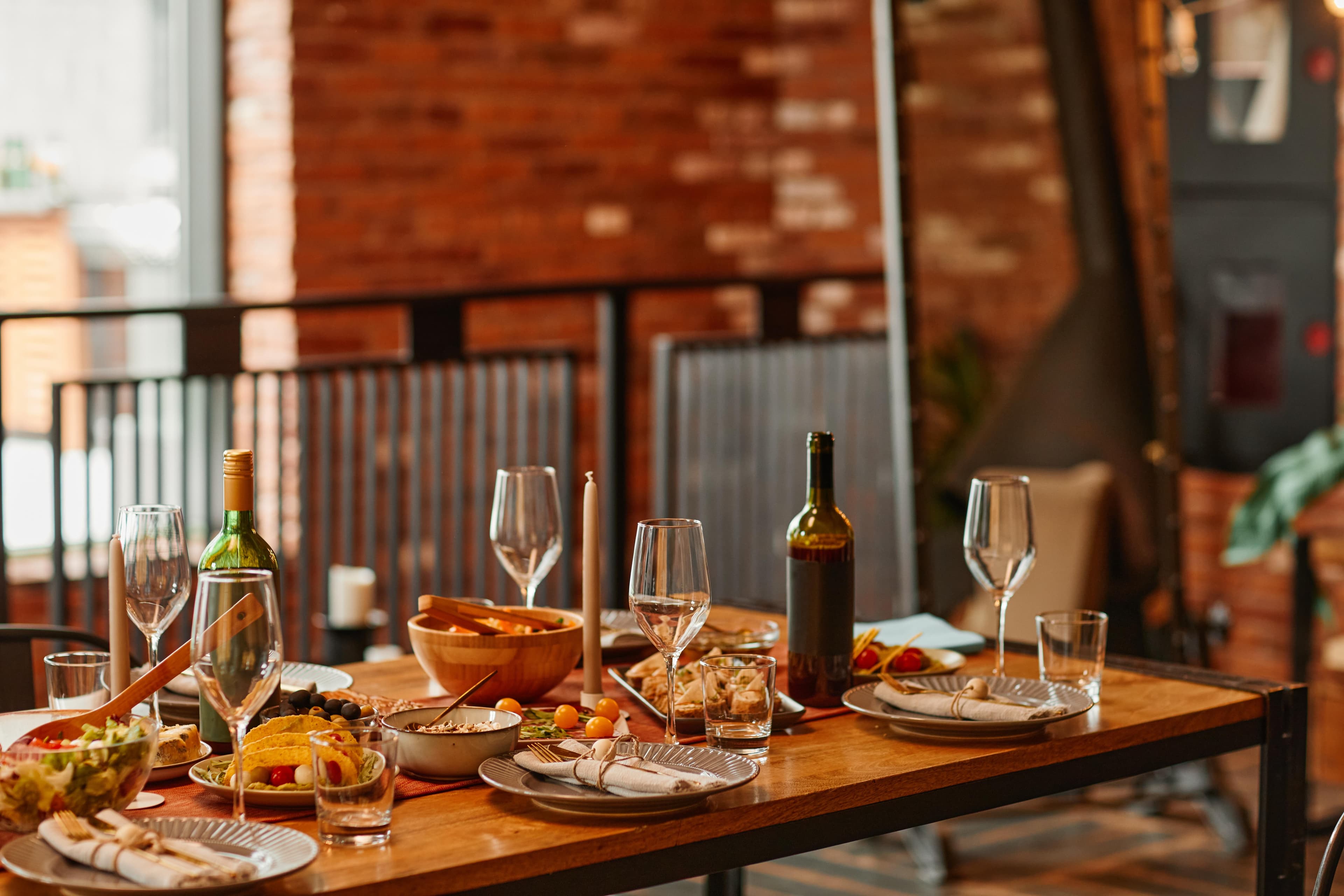Ein gedeckter Esstisch in einem Loft mit Wein, Salaten, Vorspeisen und Geschirr in gemütlichem, modernem Ambiente.