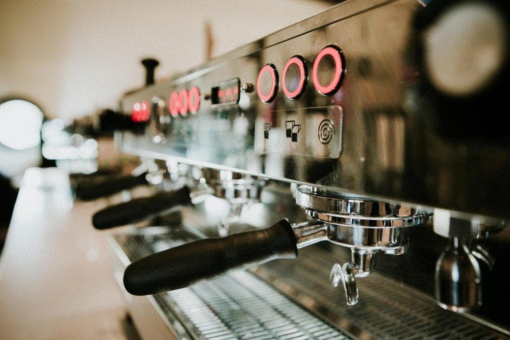 Professionelle Espressomaschine aus Edelstahl mit leuchtend roten Bedienelementen und Siebträgern in Nahaufnahme.