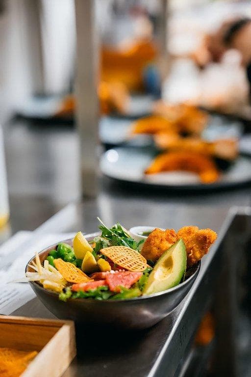 Herzhafte Bowl mit knusprigen Hähnchenstreifen, Avocado-Fächer, Edamame und gitterartigen Gemüse-Chips in einer dunklen Schale.