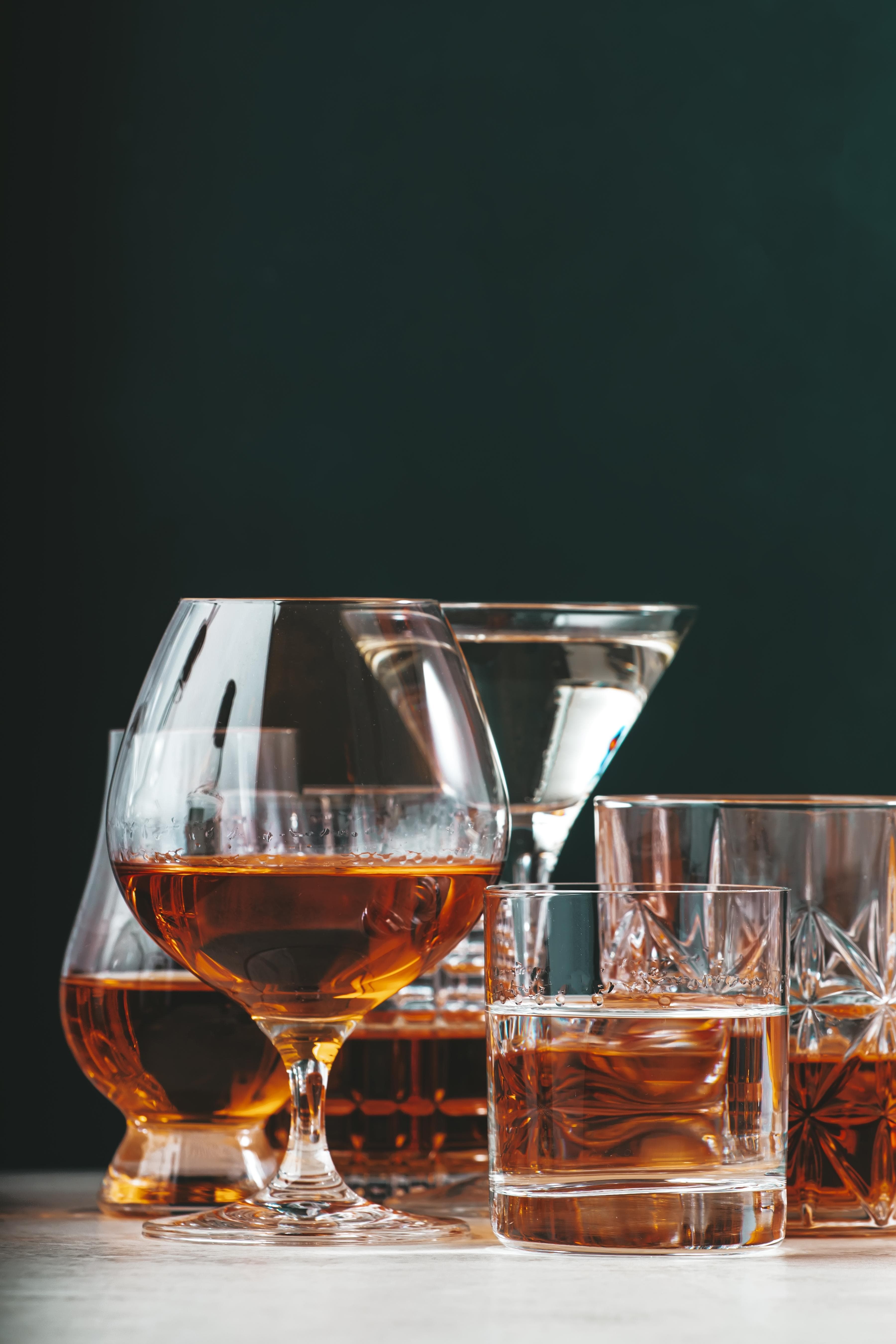 Verschiedene Gläser mit bernsteinfarbenem Whiskey und Cognac vor einem dunklen Hintergrund in eleganter Studiobeleuchtung.